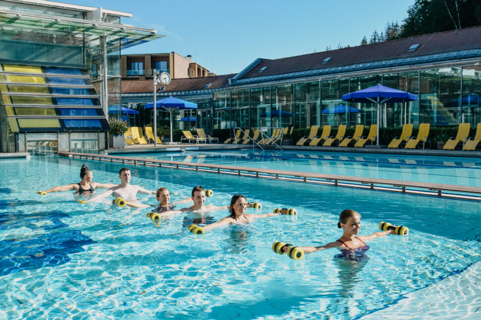 Eine Gruppe von 6 Personen mit ausgestreckten Armen mit Wasser-Hanteln beim Aqua-Sport